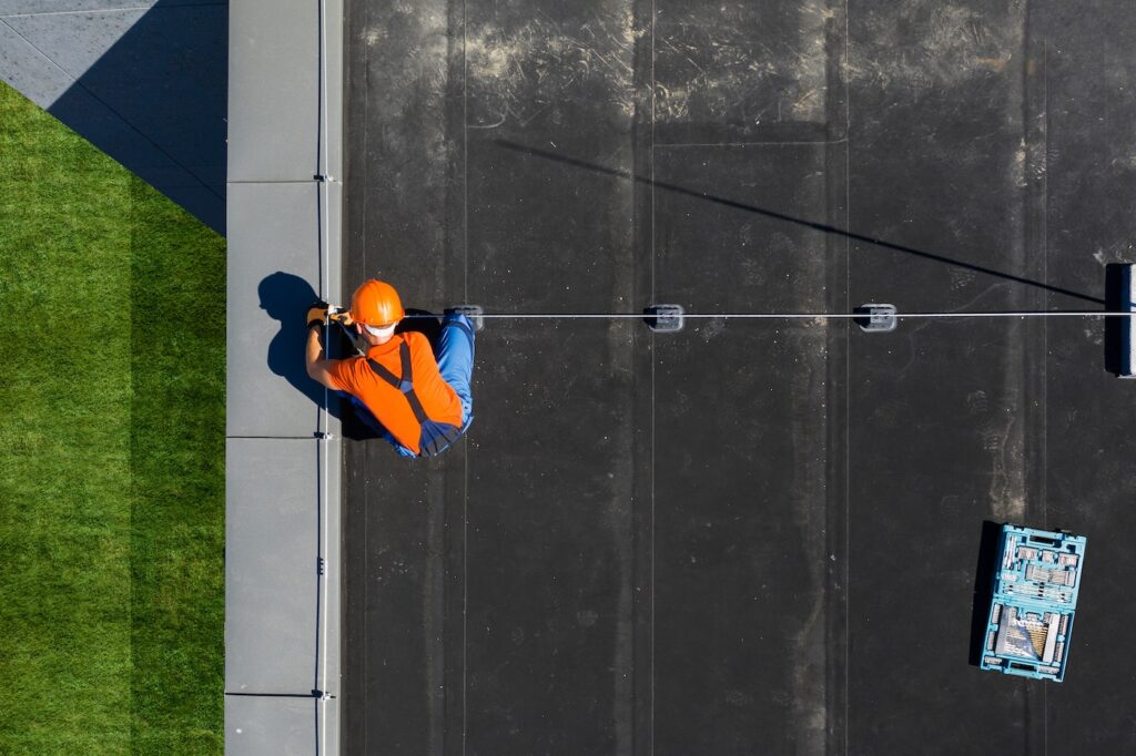 Technician Wearing Orange Uniform and Hard Hat Installing Lightning Protection System Rod on Top of Commercial Building. Protect Structure From Elements.