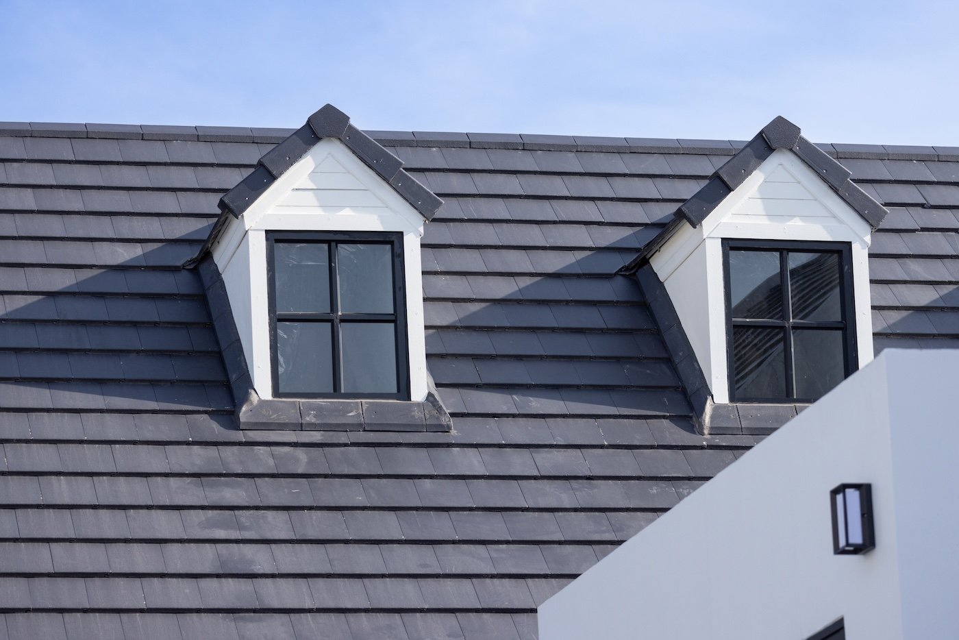Two windows on a roof with a blue sky in the background. The roof is made of metal and has a slanted design