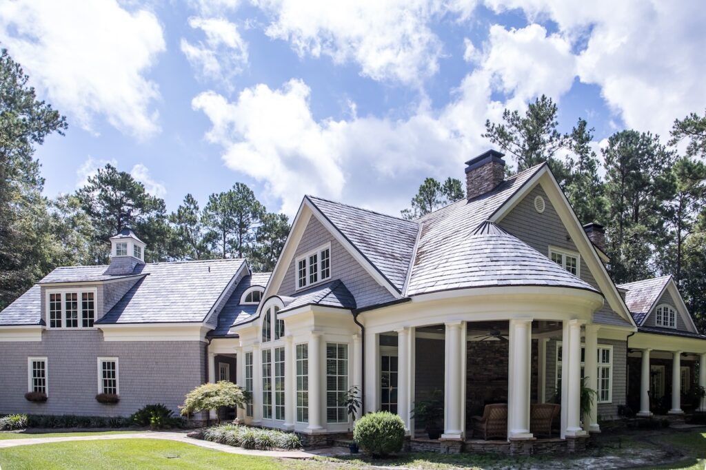 Rear view and backyard of large cape cod style home with columns and windows and a round porch patio
