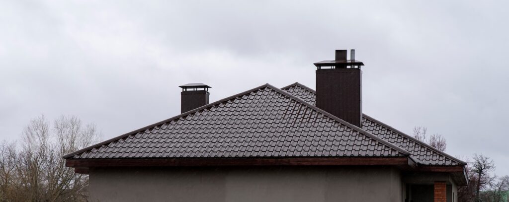 Wet brown metal roof with two chimneys