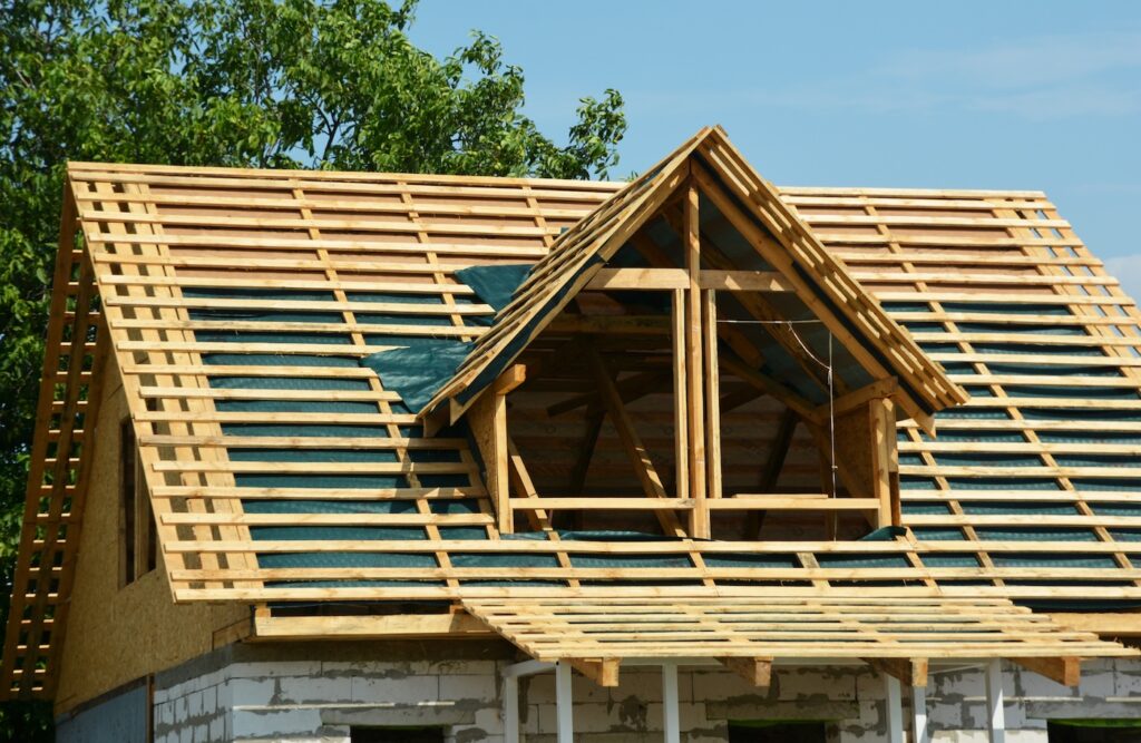 Roofing construction with damp proofing. Installing a new vapor barrier roof underlay and timber battens on a framing roof with a mansard roof window before tiles installation.