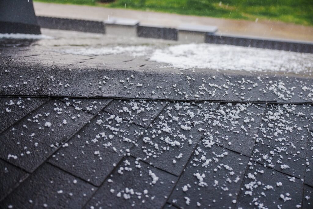 Small hailstones falling and covering a dark shingled roof during a rainstorm. High quality photo