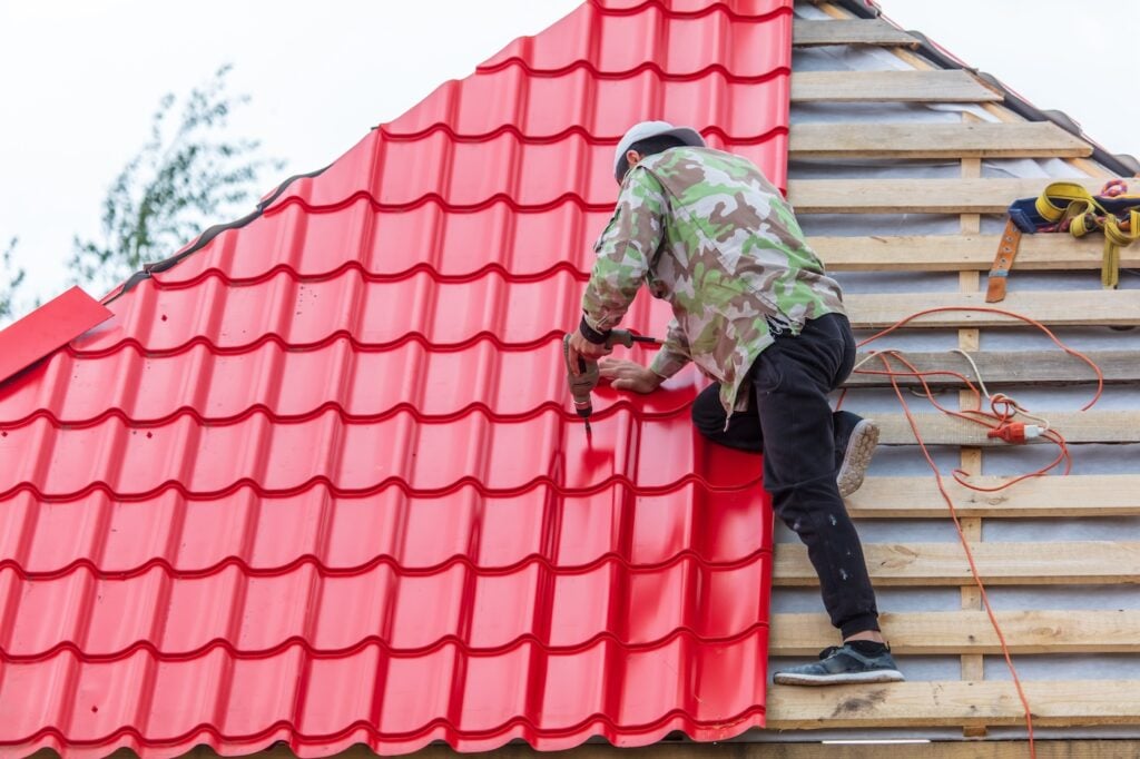 Workers install red metal tiles on the roof of the house.