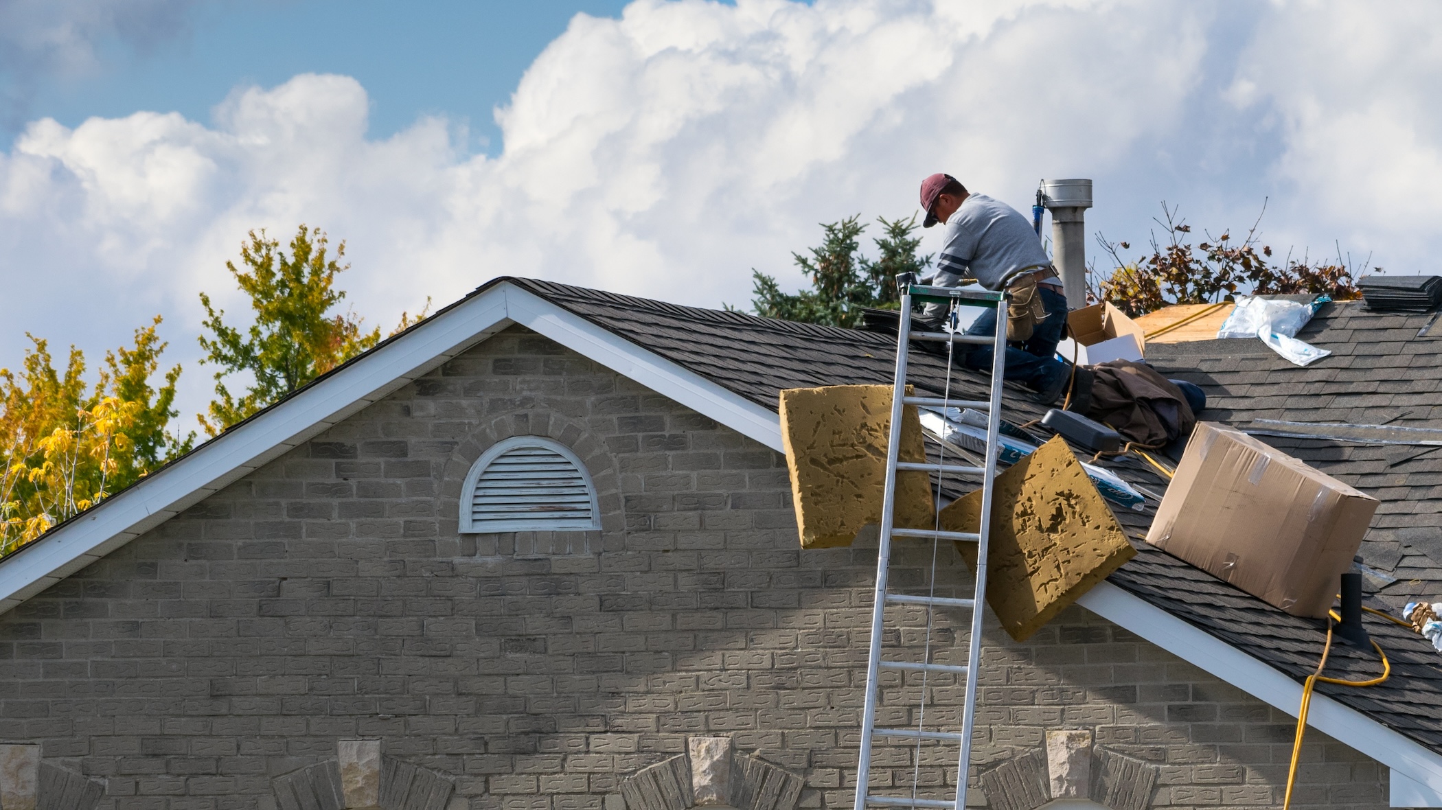 Worker on the roof of a 2-story family house installing new asphalt shingles
