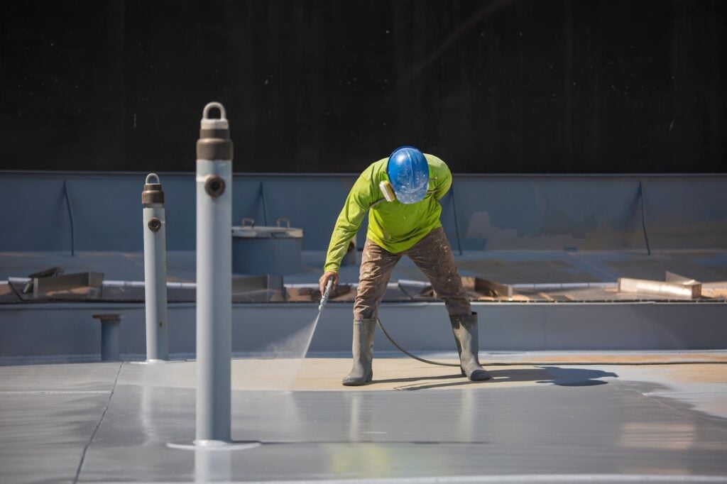 A male worker holding an industrial spray gun used for roof plate tank surface on steel industrial painting