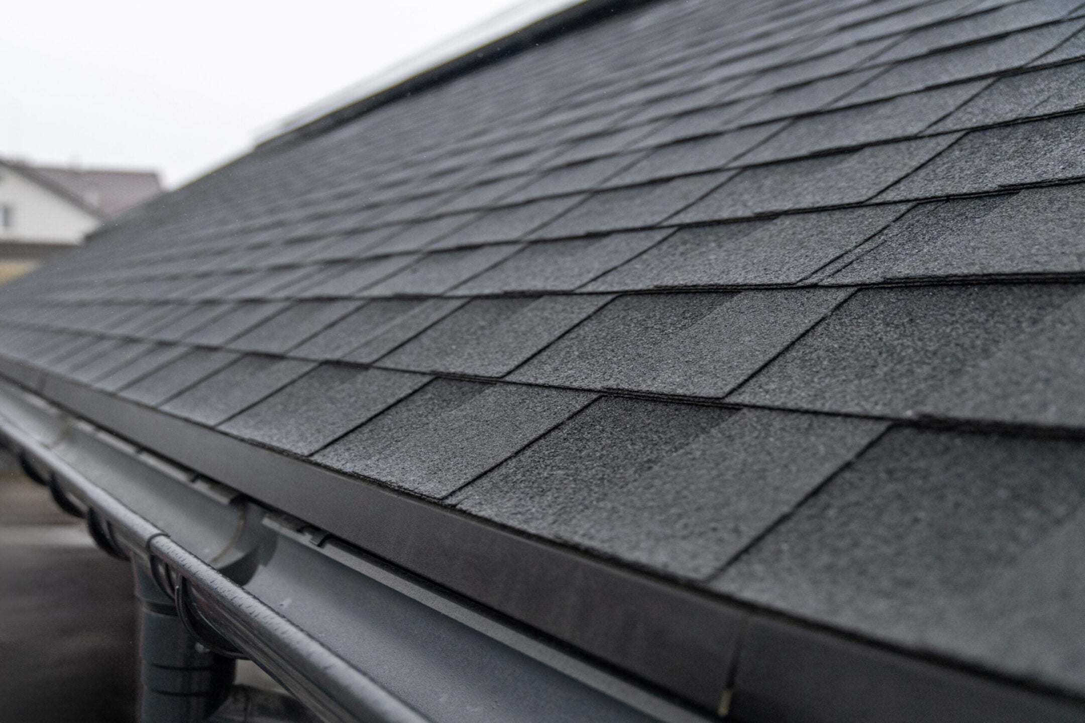 Dark gray asphalt roof shingles with rain gutter system close up