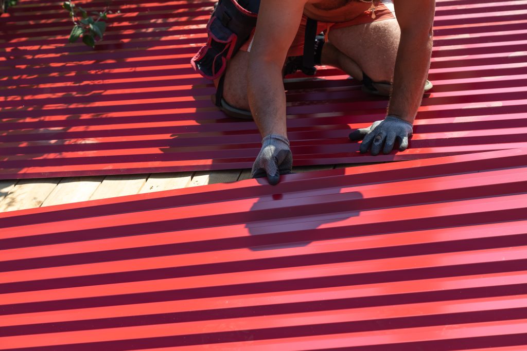 corrugated metal roofing A man screws sheets of corrugated board on the roof with a screwdriver. Repair and replacement of the roof. Laying of corrugated sheets